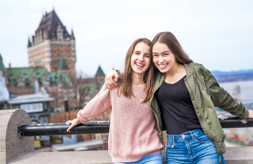 Two people leaning on a railing overlooking Old Quebec, with Château Frontenac and the St. Lawrence River in the background.